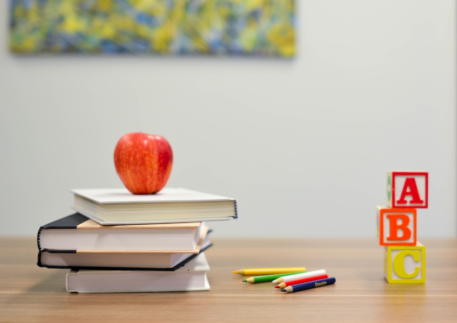 Ein Apfel ist auf einem Stapel Bücher neben Stiften und 3 Holzwürfeln auf denen A, B und C zusehen ist.