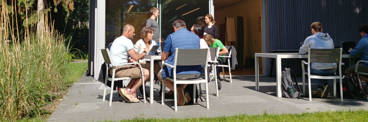 Mehrere Lehrkräfte sitzen auf der Terrasse eines Veranstaltungsorts und arbeiten konzentriert an Tischen